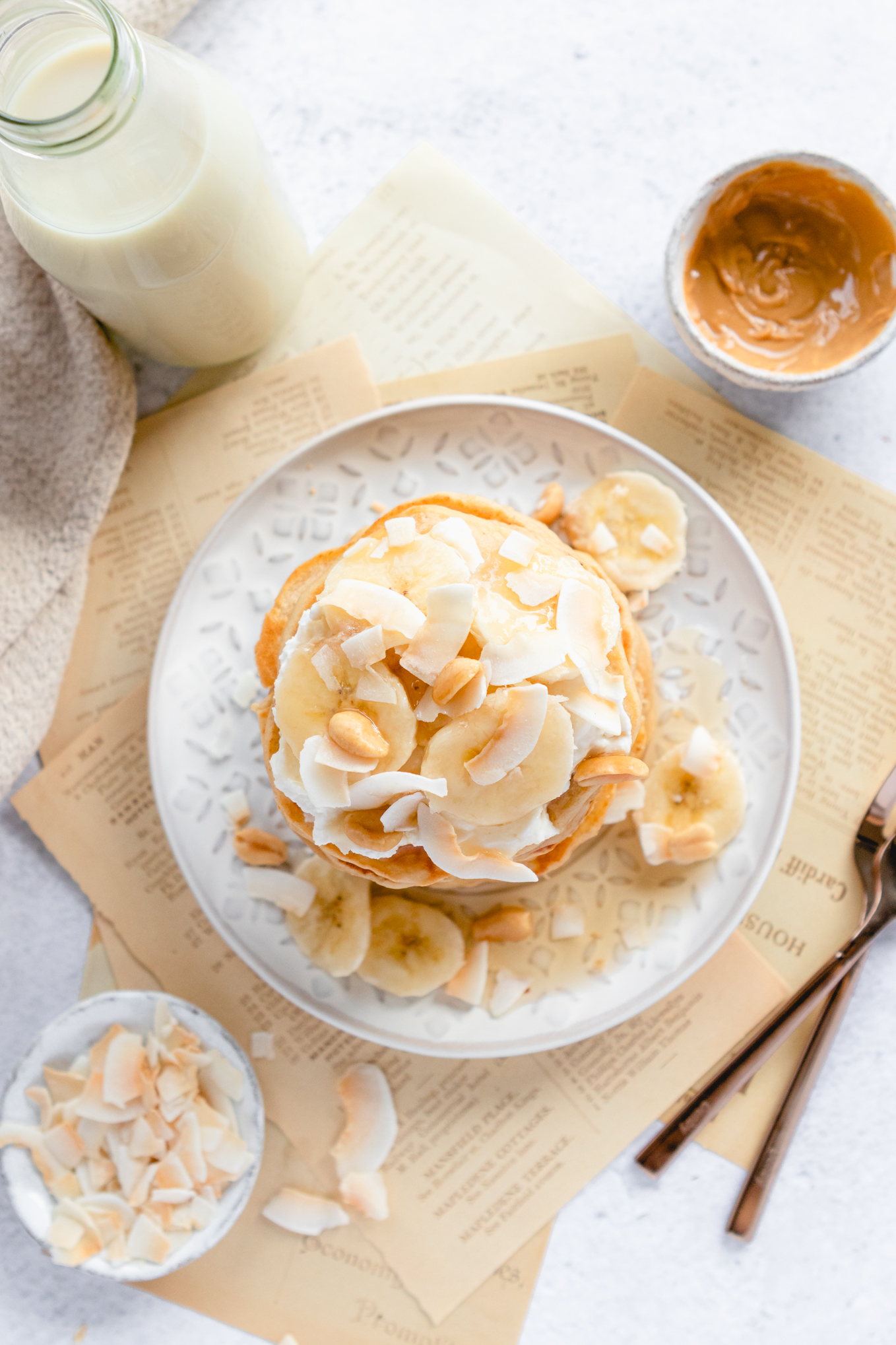 Peanut Butter Pancakes on a plate, with a glass of milk and bowl of peanut butter and coconut flakes on the side. 