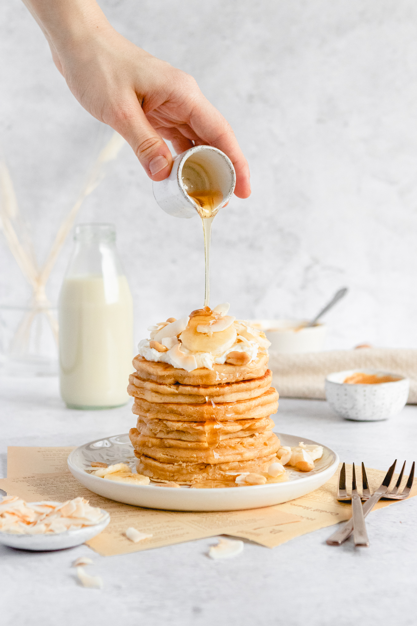 hand pouring syrup over pancakes